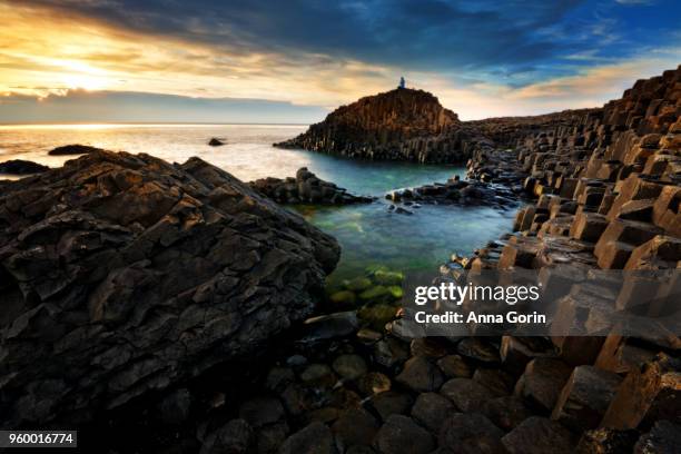 lone silhouetted tourist on top of basalt columns forming famous giant's causeway in northern ireland, long exposure at sunset - bushmills stock pictures, royalty-free photos & images