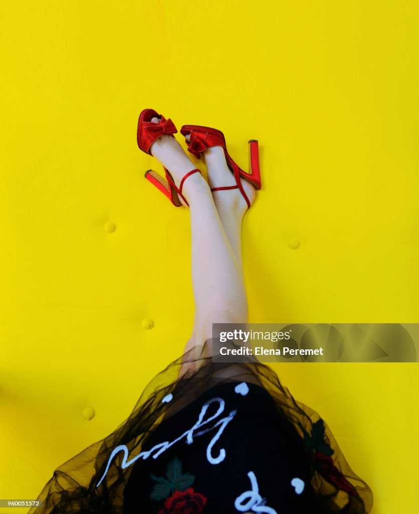 Woman's Legs Up  wearing Red High Heels on yellow background