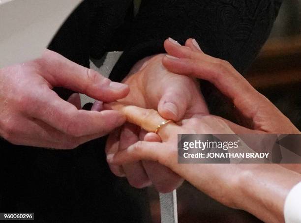 Britain's Prince Harry, Duke of Sussex, places the wedding ring on the finger of US fiancee of Britain's Prince Harry Meghan Markle during their...