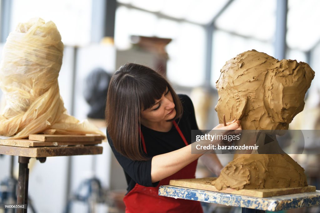 Jonge vrouwelijke beeldhouwer werkt in haar atelier