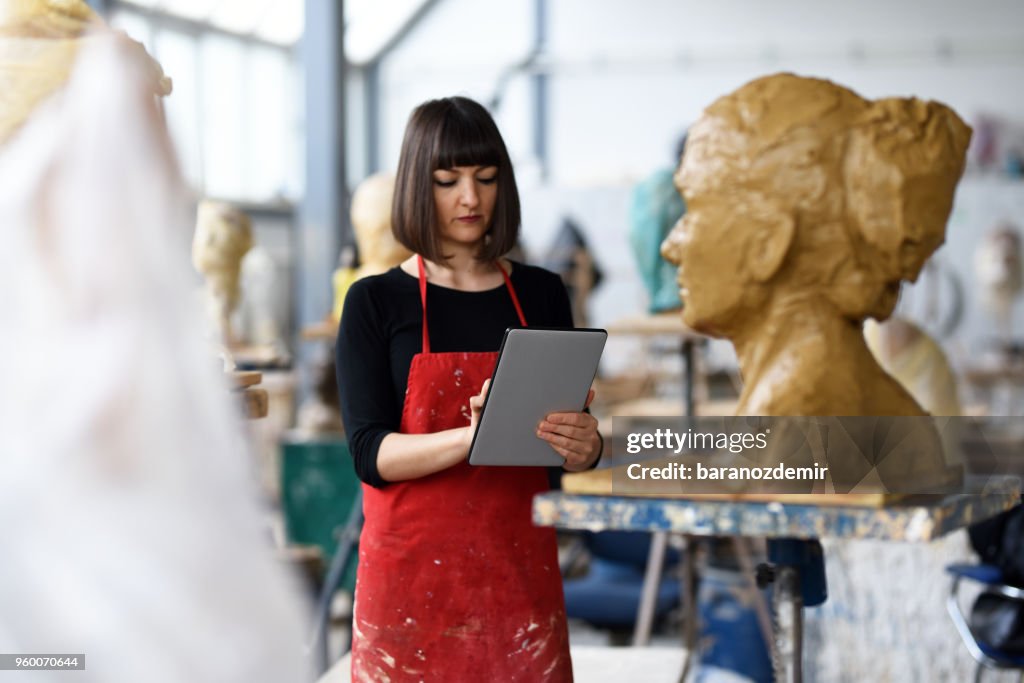 Jeune femme sculpteur travaille en collaboration avec tablette numérique dans son atelier