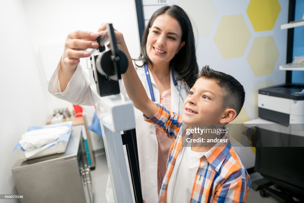 Menino bonito, ajudando o pediatra feminina para ajustar a escala de peso ambos olhando muito feliz