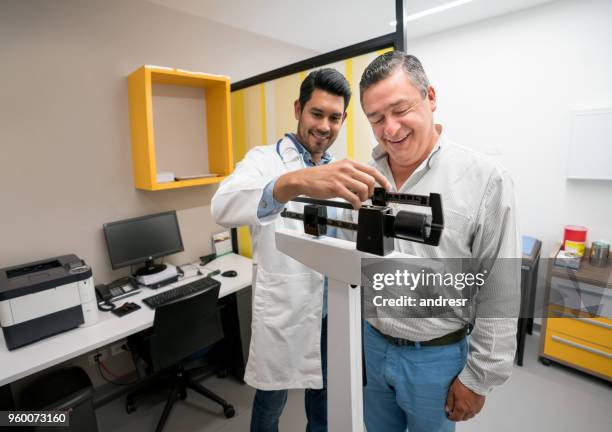 cheerful mid adult patient getting a check up and doctor adjusting the scale to measure his weight both smiling - doctor's office scale stock pictures, royalty-free photos & images