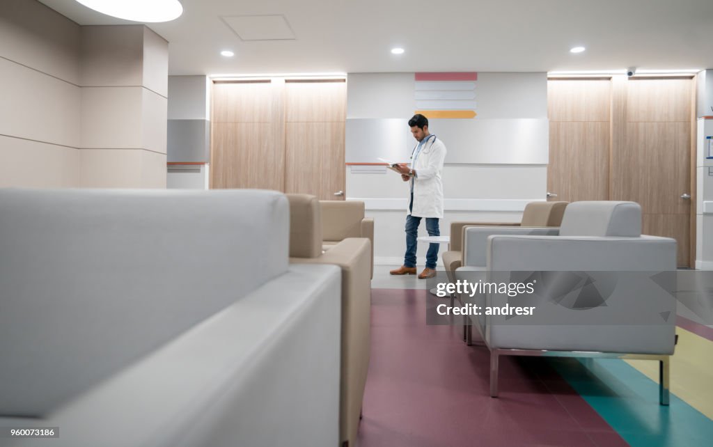 Docteur debout près de la salle d’attente en regardant une fiche médicale très concentré