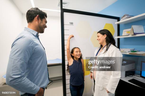 playful little girl at the pediatrician making herself taller and doctor and dad laughing - high up stock pictures, royalty-free photos & images