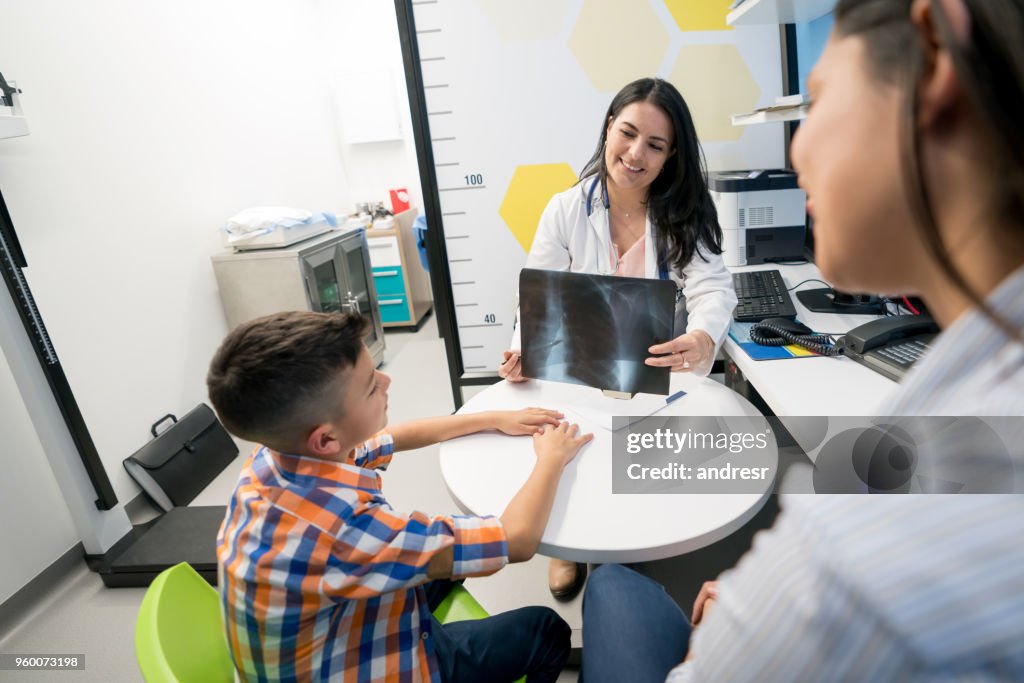 Madre e hijo hablando con mujer pediatra y médico que muestra al niño una radiografía de su