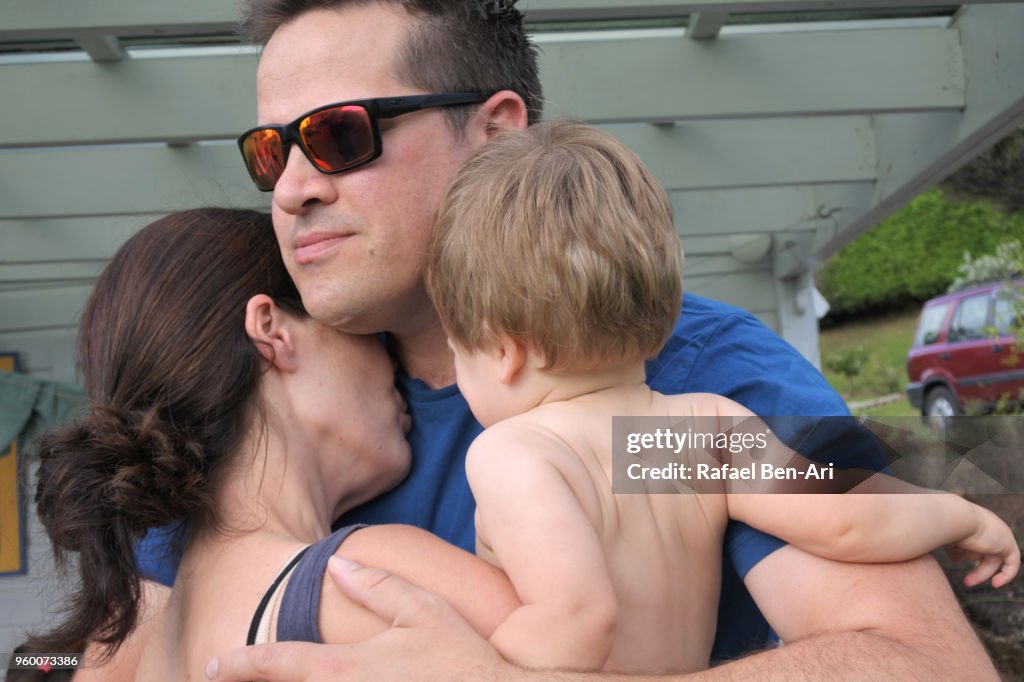 Father hugs his wife and baby (age 01) before driving away from home
