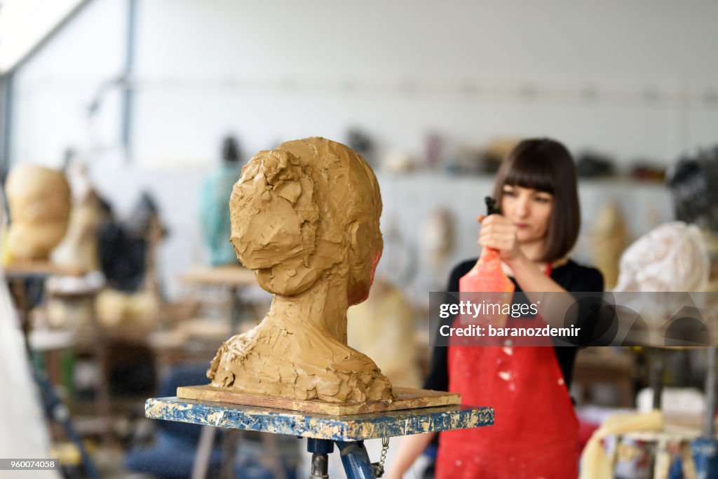 Jovem escultor feminino está trabalhando em seu estúdio