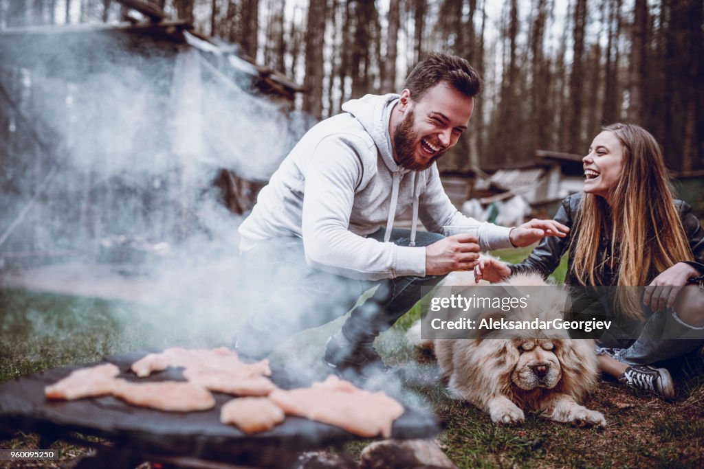 Couple Campers Making Barbecue And Having Fun With Dog