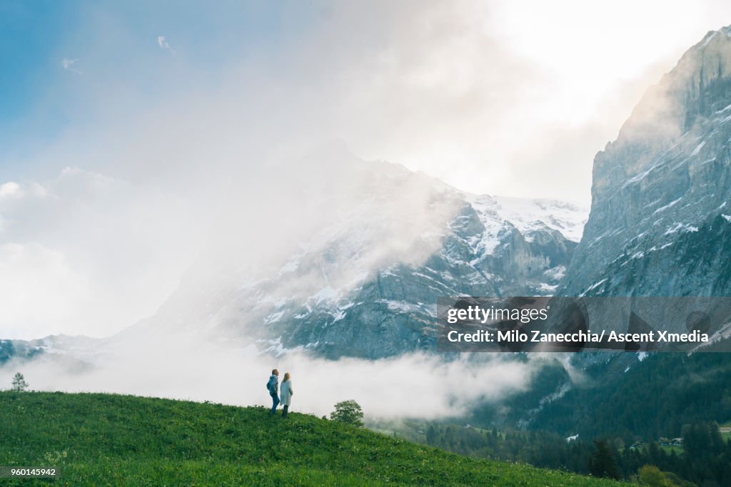Mature couple walk into meadow, look towards mountains