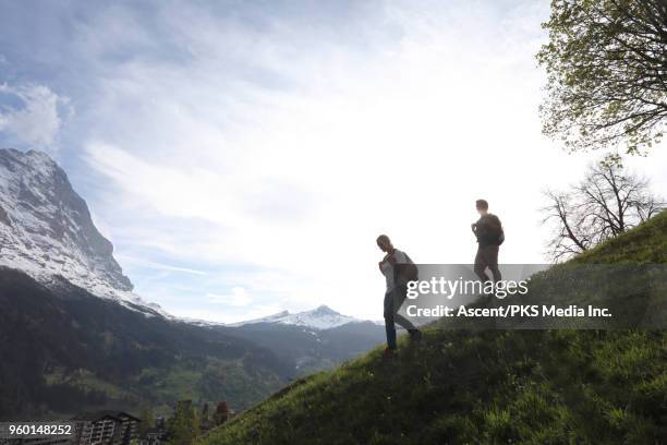 hiking couple descend meadow slope, look towards mountains - shorts down stock pictures, royalty-free photos & images