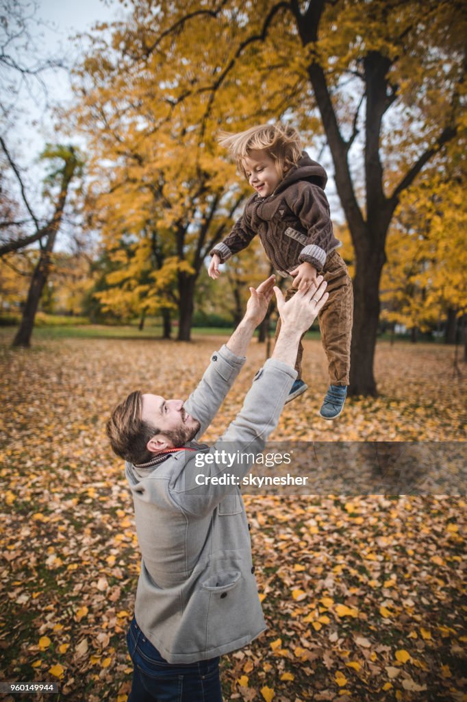 Playful father throwing his small son high up in autumn day.