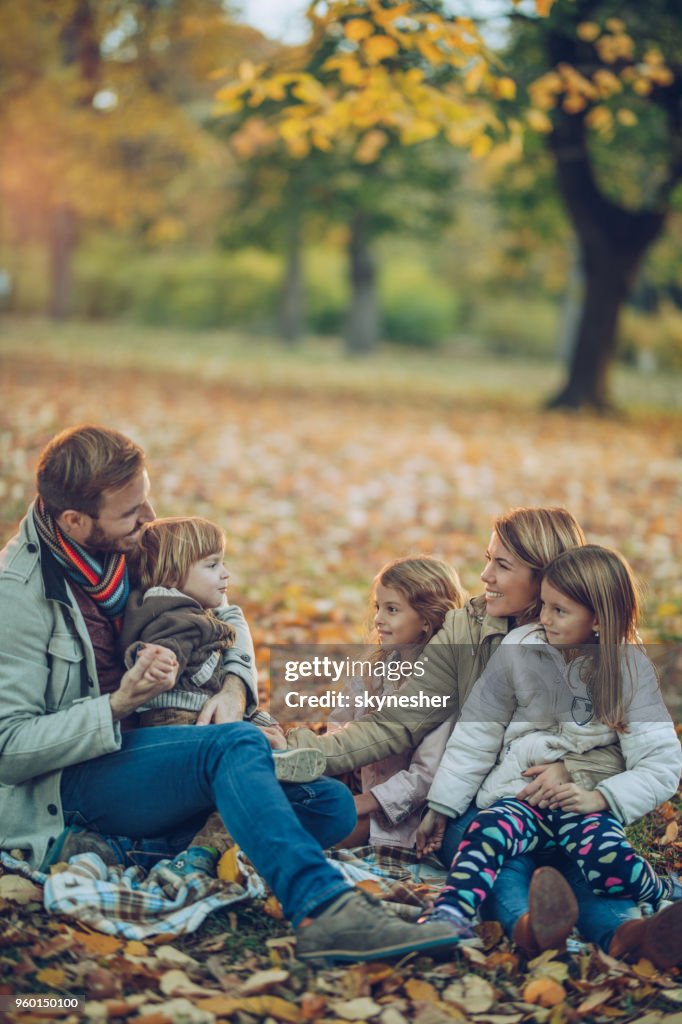 Felices padres y sus tres hijos hablando mientras se relaja en el parque de otoño.