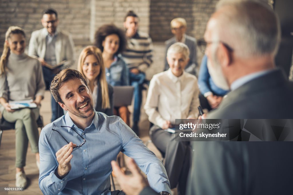 Happy entrepreneurs talking to public speaker on a seminar in a board room.