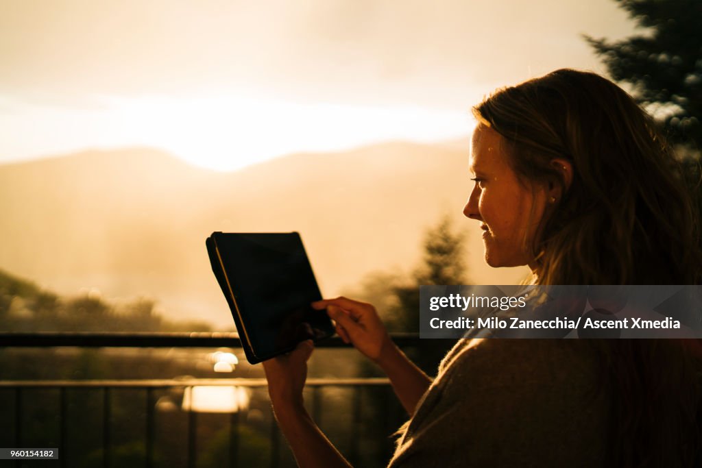 Woman uses digital tablet against backdrop of sunrise