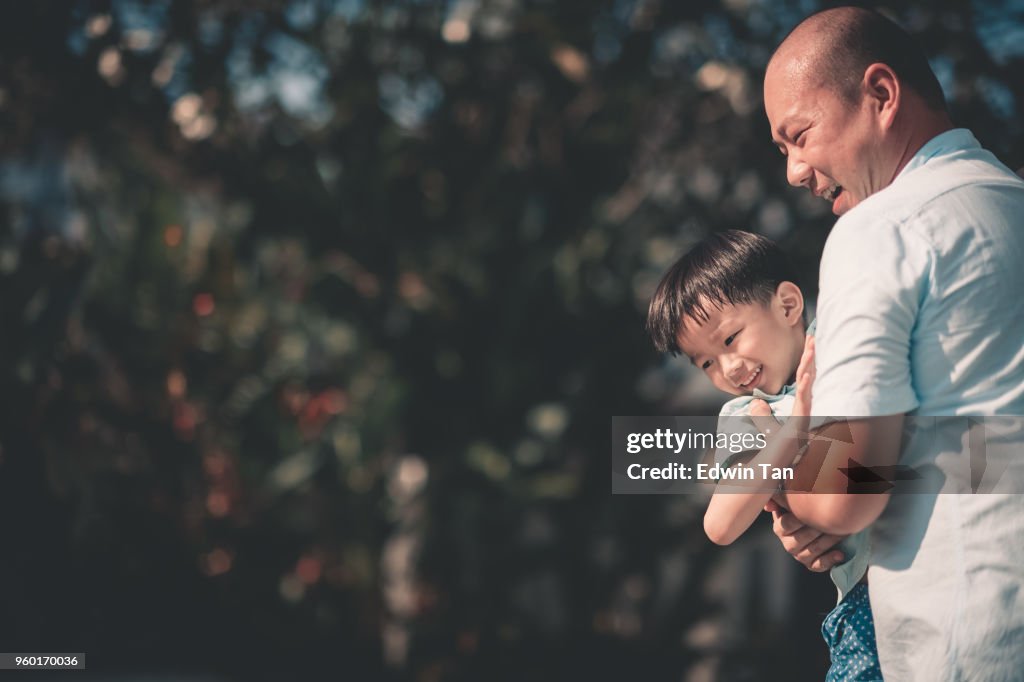楽しい時を過す中国のアジアの家族の息子を運ぶ彼らの家の父の前で時間を結合