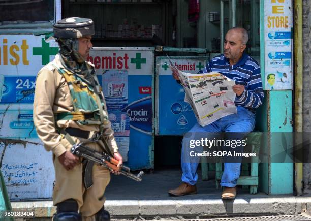 Kashmiri man reads a newspaper as an Indian paramilitary trooper stands guard during restrictions imposed ahead of Indian PM Narendra Modi's visit in...