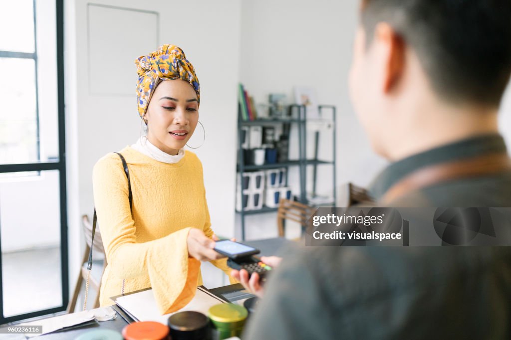 Young Woman Paying with Smartphone in a Cafe
