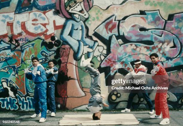 Teenagers breakdancing next to a wall covered in grafitti, Brooklyn, New York, April 1984.