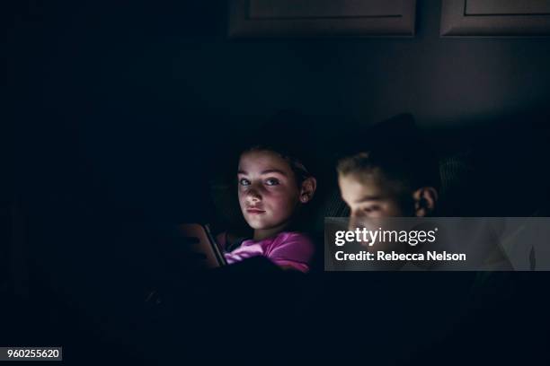 set of boy and girl twins using digital tablets in dark room at night - digital twin bildbanksfoton och bilder