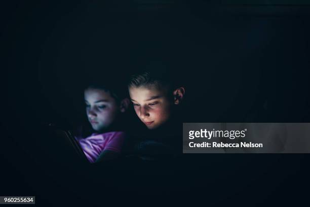 set of boy and girl twins using digital tablets in dark room at night - digital twin bildbanksfoton och bilder