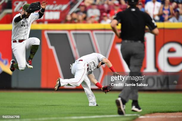 Jesse Winker of the Cincinnati Reds leaps to avoid colliding with Scooter Gennett of the Cincinnati Reds after Gennett was unable to chase down a...