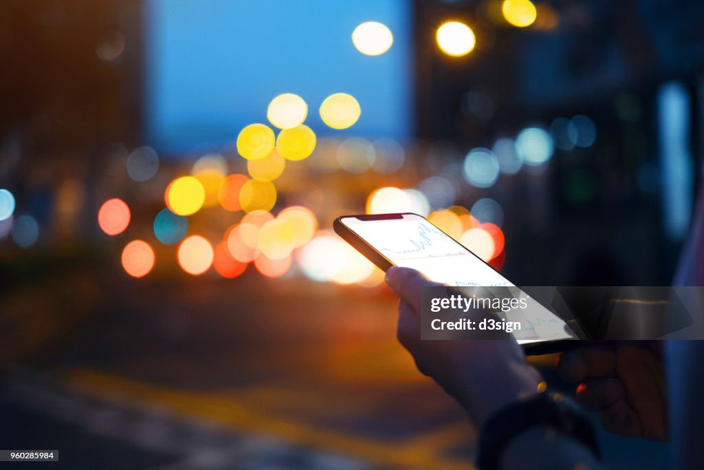 Close up of hands checking financial trading data on smartphone in city street at night