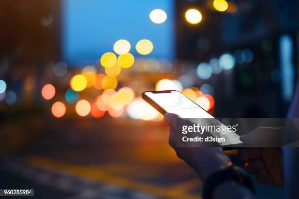 close up of hands checking financial trading data on smartphone in city street at night - big tech stock pictures, royalty-free photos & images