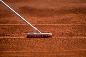 Worker cleans a line of tennis court with a brush