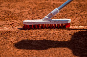 Worker cleans a line of tennis court with a brush