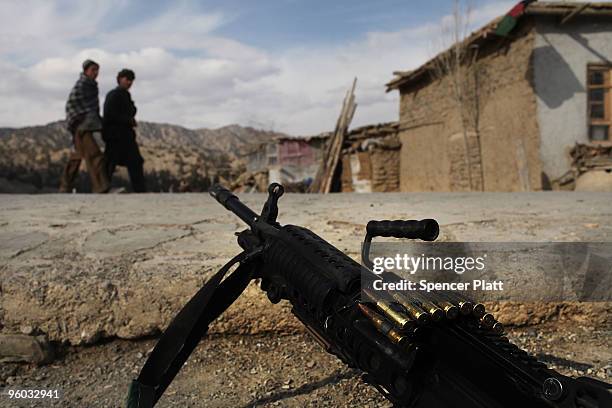 Teens walk by a weapon belonging to members of the US Army Able Company, 3-509 Infantry Battalion who are patrolling the main street of Zerak January...