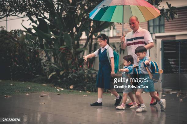 asian chinese family father receiving children back from school in rain in front of their home - asia rain stock pictures, royalty-free photos & images