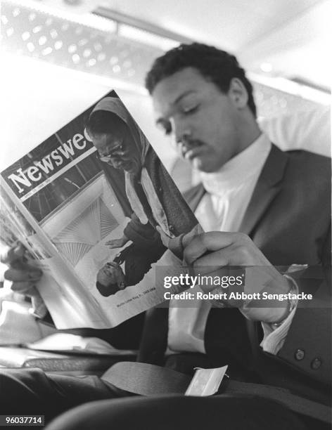 Jesse Jackson takes a moment to read a copy of Newsweek magazine, with a cover showing a mourner passing by the body of the recently assassinated Dr....