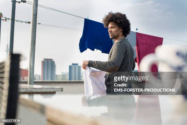 single men is hanging out the laundry on his rooftop - afro man washing stock pictures, royalty-free photos & images
