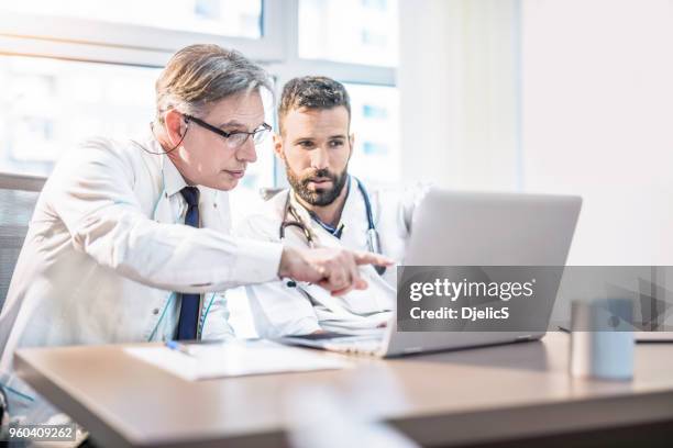 twee artsen medische grafieken kijken op laptop. - two doctors talking stockfoto's en -beelden