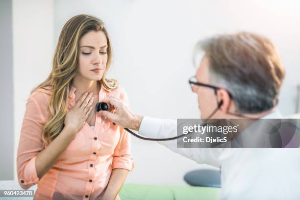 junge frau bekommt ihre schmerzhafte brust von einem arzt untersucht. - stethoscope heart stock-fotos und bilder