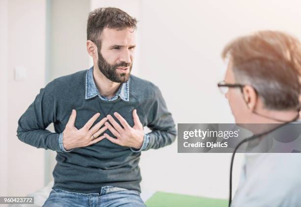 mid volwassen mannelijke patiënt met een beschrijving van een pijn op de borst zijn arts. - borstkas stockfoto's en -beelden