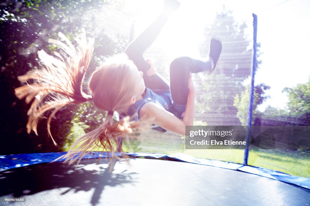 Girl (10-11) doing a somersault on a trampoline