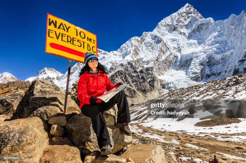 Young woman studying map next to signpost, Nepali Himalaya