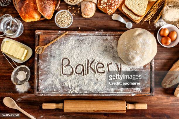 ambachtelijke bakkerij: bakkerij teken op de snijplank. vers gemengde bun, rollen en ingrediënten - flour bag stockfoto's en -beelden