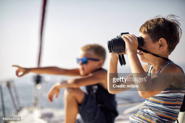 garçons assis sur le pont et à l’aide de jumelles alors qu’il naviguait - miljko photos et images de collection