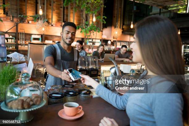 woman making a contactless payment at a restaurant - contactless payment stock pictures, royalty-free photos & images