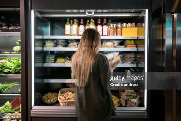 vrouw koopt voedsel bij de supermarkt - fridge full of food stockfoto's en -beelden