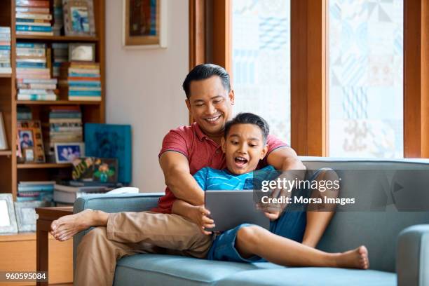 vader en zoon met behulp van digitale tablet op bank - malaysia father and son stockfoto's en -beelden