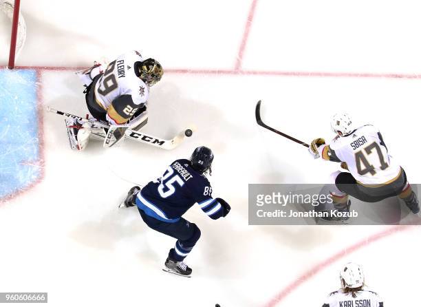Goaltender Marc-Andre Fleury of the Vegas Golden Knights makes a stick save as Mathieu Perreault of the Winnipeg Jets and teammate Luca Sbisa eye the...