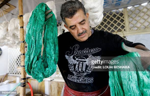 Mohammad al-Rihawi dips silk threads into green dye on January 23, 2018 at his atelier in the Syrian capital Damascus. Civil war has ravaged Syria...