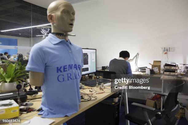 An employee works while a GRAS Sound & Vibration A/S KEMAR head and torso simulator for hearing aid testing manikin stands in the headphones testing...