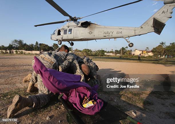 Army soldiers from the 82nd Airborne cover up an injured women as a Navy helicopter lands to medivac her after she was injured during the earthquake...