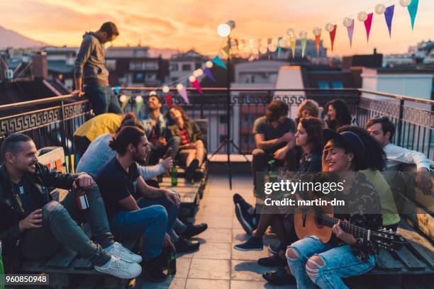 friends drinking beer and playing the guitar on rooftop party - martin guitar stock pictures, royalty-free photos & images