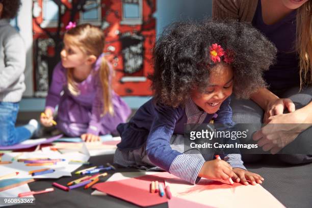 cheerful girl drawing on paper while sitting by teacher at preschool - kunst en nijverheid stockfoto's en -beelden